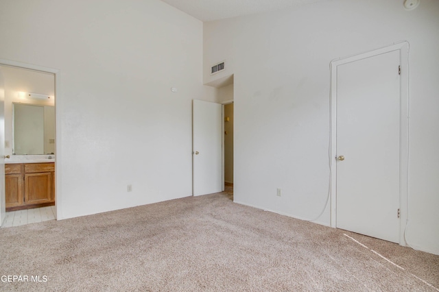 unfurnished bedroom with connected bathroom, visible vents, carpet floors, and high vaulted ceiling