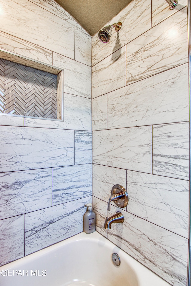 bathroom featuring a textured ceiling and tiled shower / bath