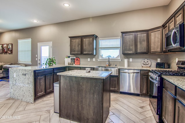 kitchen featuring stainless steel appliances, light stone counters, light parquet floors, kitchen peninsula, and a center island