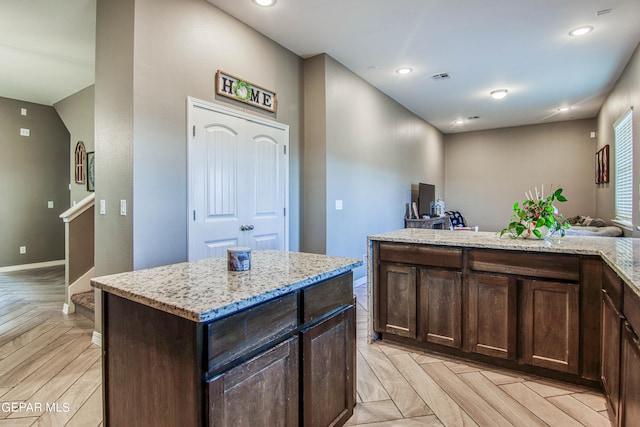 kitchen with light parquet flooring, light stone counters, a center island, and dark brown cabinetry