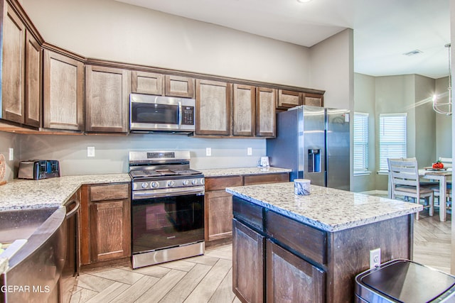 kitchen featuring a kitchen island, stainless steel appliances, light parquet flooring, and light stone countertops