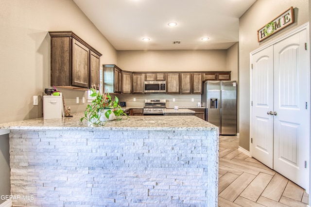 kitchen with appliances with stainless steel finishes, kitchen peninsula, light parquet flooring, and light stone countertops