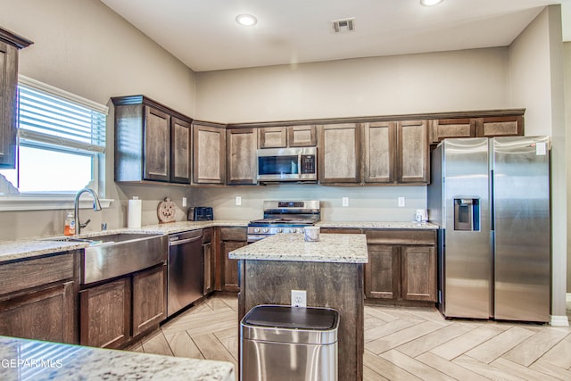 kitchen featuring a kitchen island, light stone counters, light parquet floors, sink, and stainless steel appliances