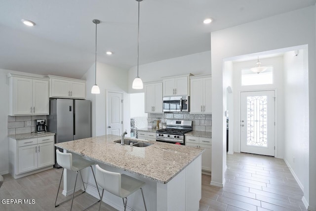 kitchen featuring tasteful backsplash, white cabinets, a kitchen island with sink, stainless steel appliances, and a sink