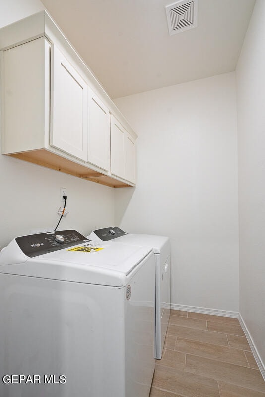 clothes washing area featuring washer and dryer, light hardwood / wood-style flooring, and cabinets