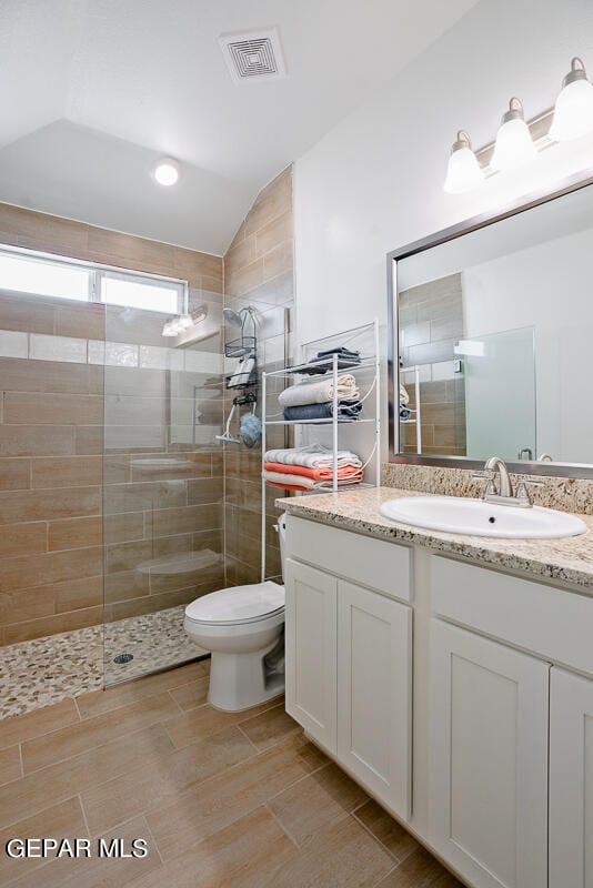 bathroom with a tile shower, toilet, vanity, tile patterned floors, and vaulted ceiling