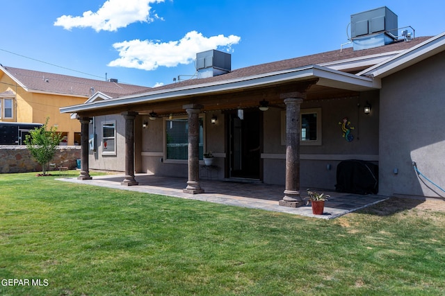 rear view of property with ceiling fan, a patio, a shingled roof, a yard, and stucco siding