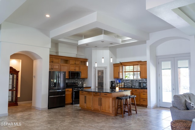 kitchen with arched walkways, open shelves, a kitchen breakfast bar, a center island, and black appliances