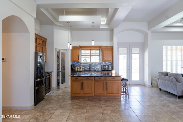 kitchen featuring decorative backsplash, black fridge with ice dispenser, dark countertops, a kitchen island, and a tray ceiling