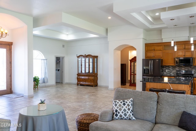 living area featuring arched walkways, a chandelier, light tile patterned flooring, a towering ceiling, and a raised ceiling