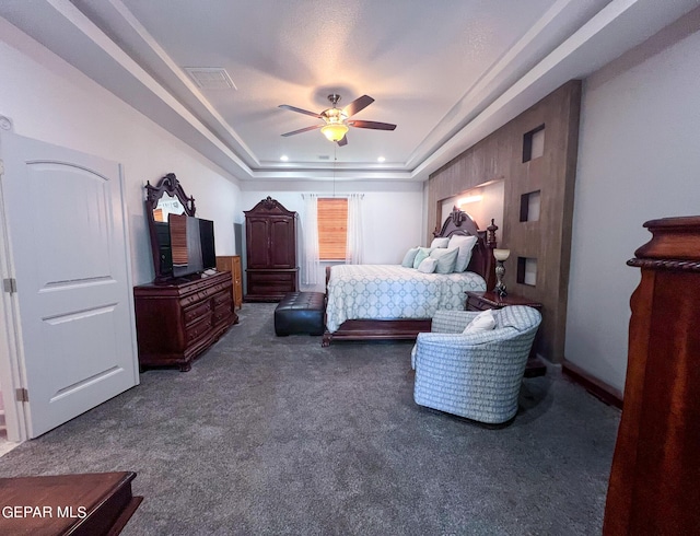 bedroom with dark carpet, a raised ceiling, visible vents, and a ceiling fan