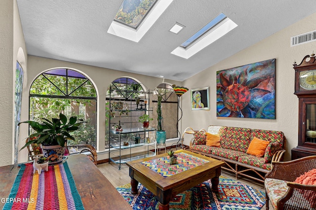 living room with visible vents, a textured wall, a textured ceiling, wood finished floors, and vaulted ceiling with skylight