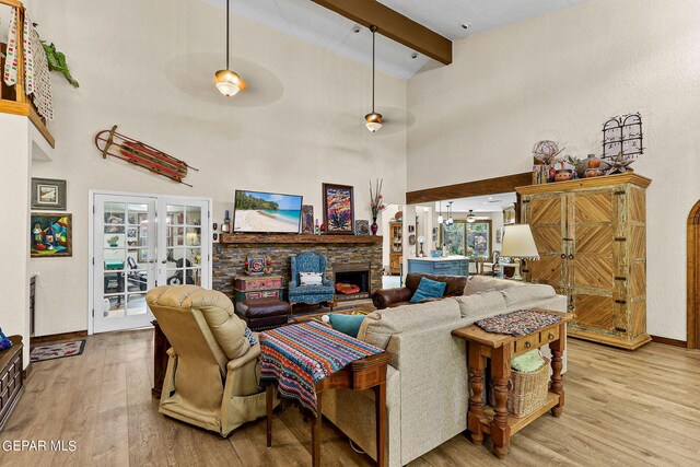 living room with beam ceiling, light wood-type flooring, a towering ceiling, and a fireplace