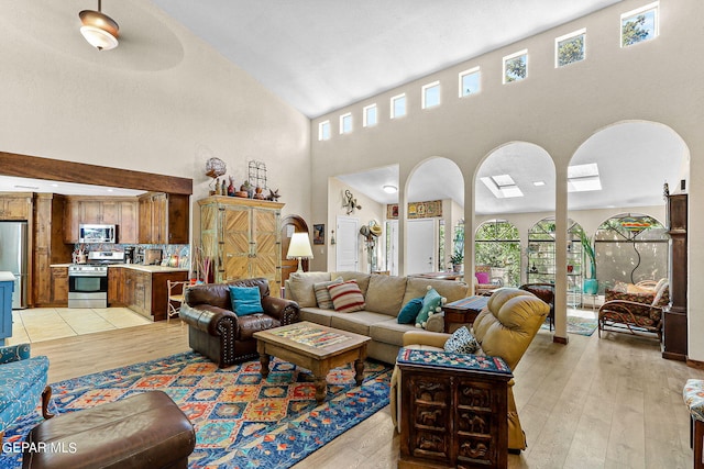 living room with a skylight, a high ceiling, and light wood finished floors