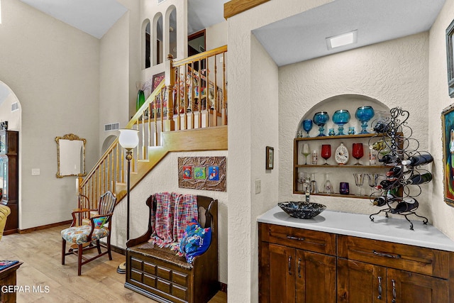 bar featuring visible vents, arched walkways, baseboards, stairs, and light wood-style floors