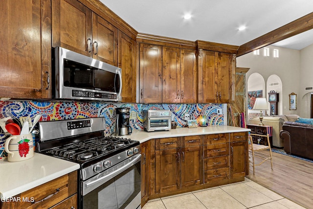 kitchen featuring decorative backsplash, beamed ceiling, light tile patterned flooring, and appliances with stainless steel finishes