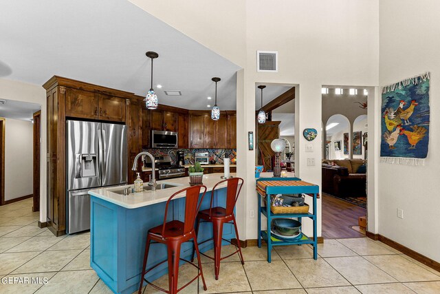 kitchen featuring stainless steel appliances, hanging light fixtures, a center island with sink, and light tile patterned flooring