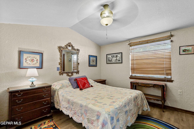 bedroom with baseboards, a textured wall, wood finished floors, vaulted ceiling, and a textured ceiling