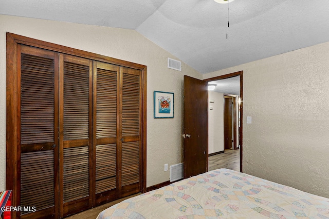 bedroom featuring lofted ceiling, visible vents, a closet, and a textured wall