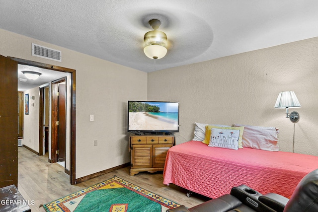 bedroom with a textured ceiling, a textured wall, wood finished floors, visible vents, and baseboards