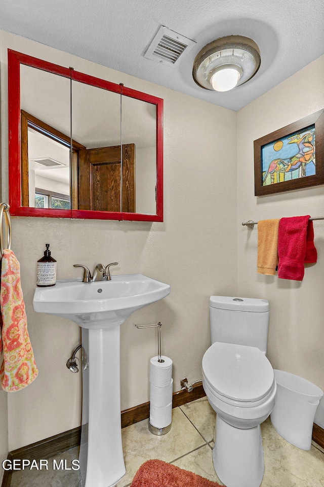 half bathroom featuring baseboards, visible vents, a textured ceiling, and toilet