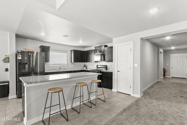 kitchen with a kitchen breakfast bar, a kitchen island, light carpet, light stone counters, and stainless steel appliances