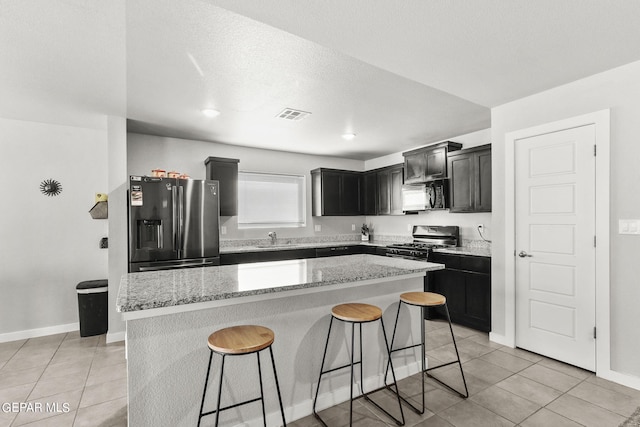 kitchen with stainless steel appliances, sink, a kitchen breakfast bar, light stone countertops, and a kitchen island