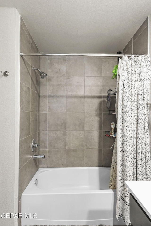 bathroom with a textured ceiling, vanity, and shower / bathtub combination with curtain