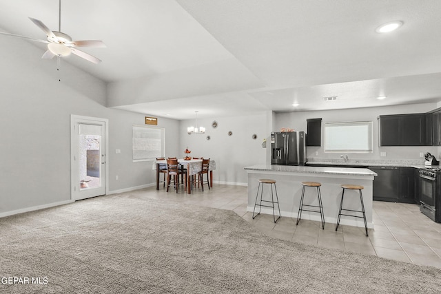 kitchen featuring ceiling fan with notable chandelier, a center island, light colored carpet, and black appliances