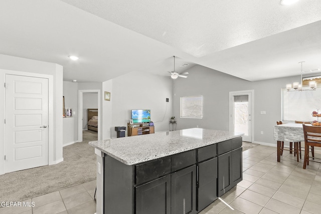 kitchen featuring decorative light fixtures, light stone counters, a kitchen island, vaulted ceiling, and light carpet