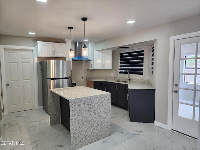 kitchen featuring sink, decorative light fixtures, wall chimney exhaust hood, stainless steel refrigerator, and white cabinets