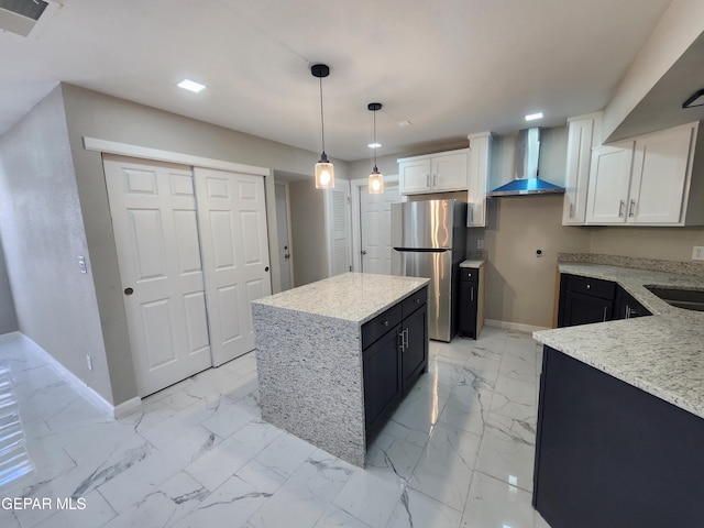 kitchen featuring white cabinetry, stainless steel refrigerator, pendant lighting, wall chimney range hood, and light tile patterned floors