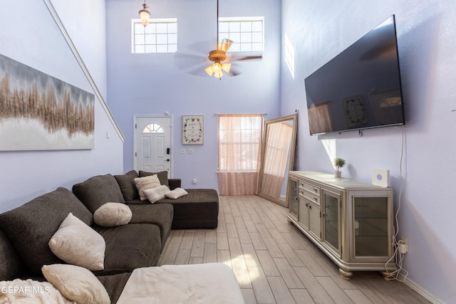 living room with a towering ceiling, light hardwood / wood-style floors, and ceiling fan