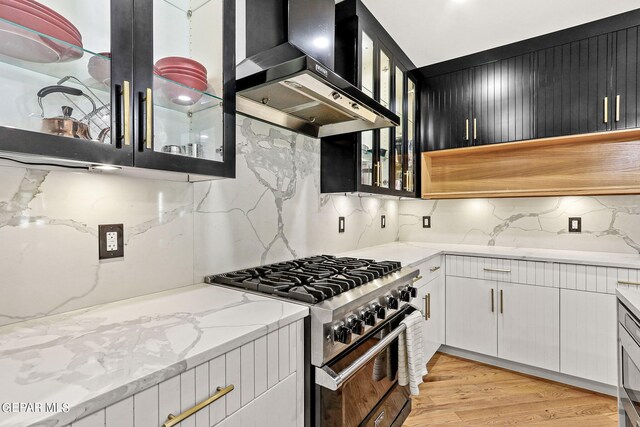 kitchen featuring white cabinets, wall chimney exhaust hood, light stone countertops, light hardwood / wood-style flooring, and high end range