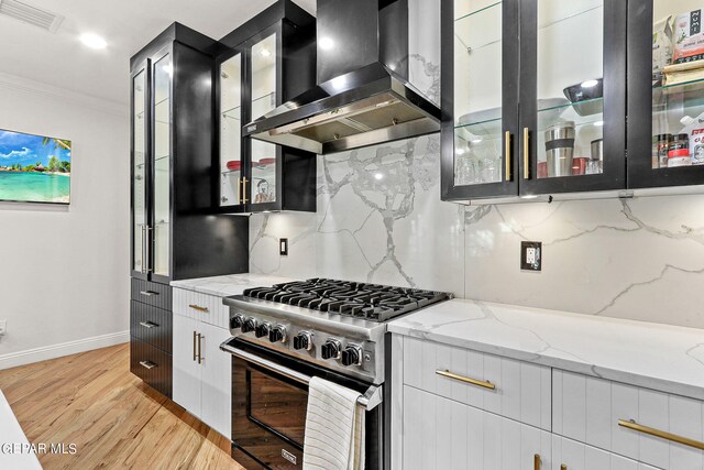 kitchen featuring light stone counters, wall chimney range hood, stainless steel range, crown molding, and light hardwood / wood-style floors