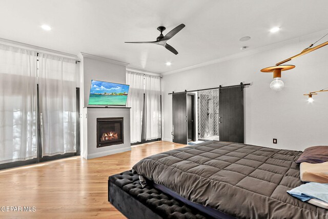 bedroom with a barn door, crown molding, ceiling fan, and light hardwood / wood-style flooring