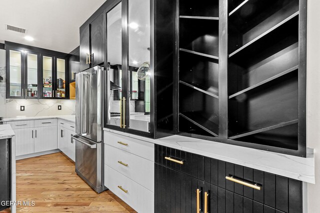 kitchen with tasteful backsplash, light hardwood / wood-style flooring, white cabinetry, stainless steel refrigerator, and light stone countertops