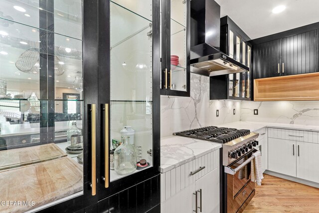 kitchen with light hardwood / wood-style floors, light stone counters, white cabinets, high end stainless steel range oven, and wall chimney range hood