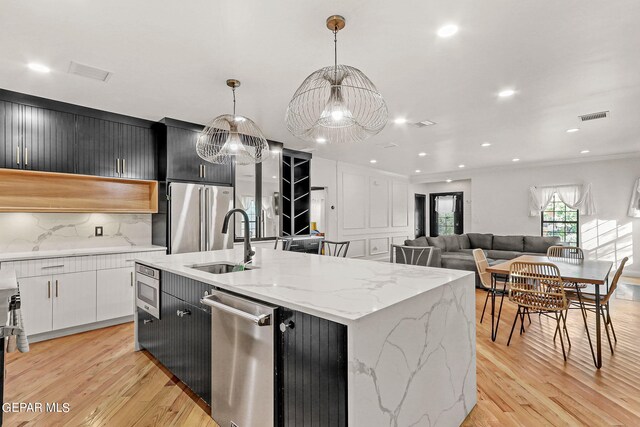 kitchen with decorative light fixtures, appliances with stainless steel finishes, a center island with sink, and sink