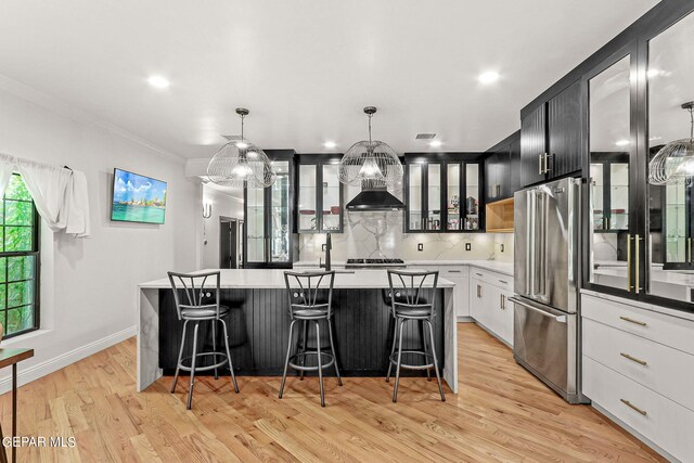 kitchen featuring light wood-type flooring, a center island with sink, appliances with stainless steel finishes, and hanging light fixtures