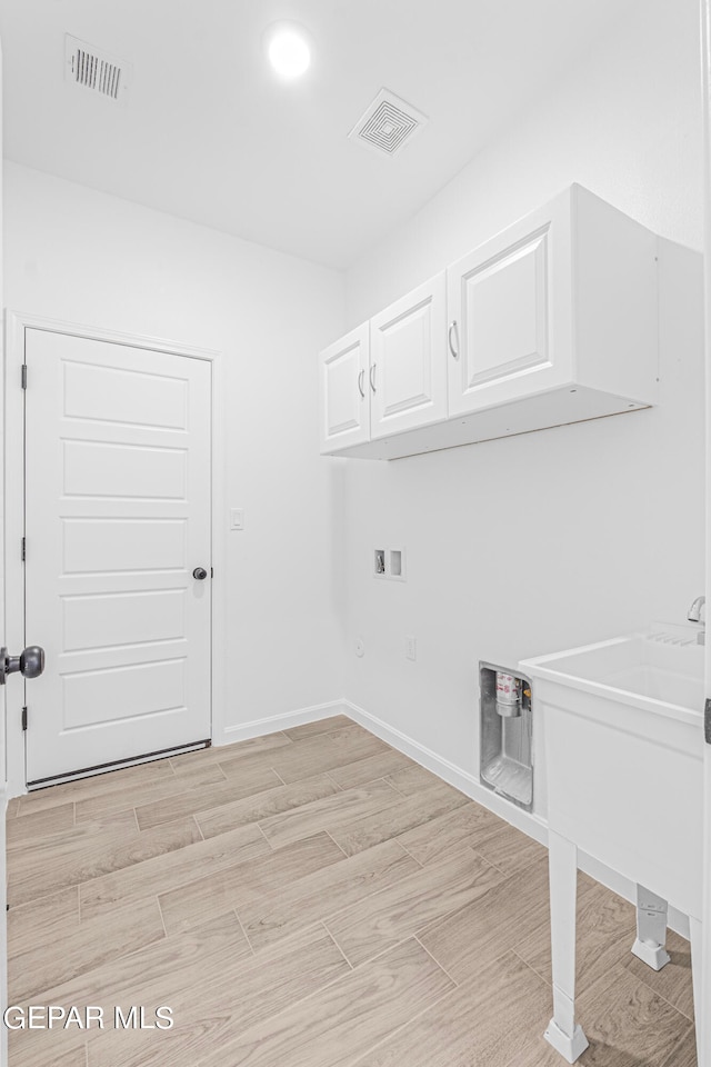 clothes washing area with cabinets, hookup for a washing machine, and light hardwood / wood-style floors