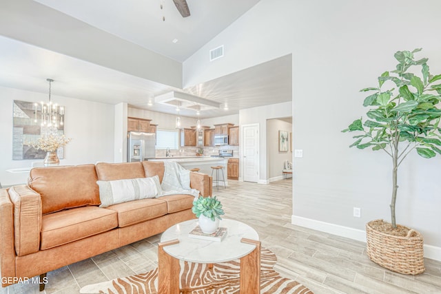 living room with ceiling fan with notable chandelier, light hardwood / wood-style flooring, lofted ceiling, and sink