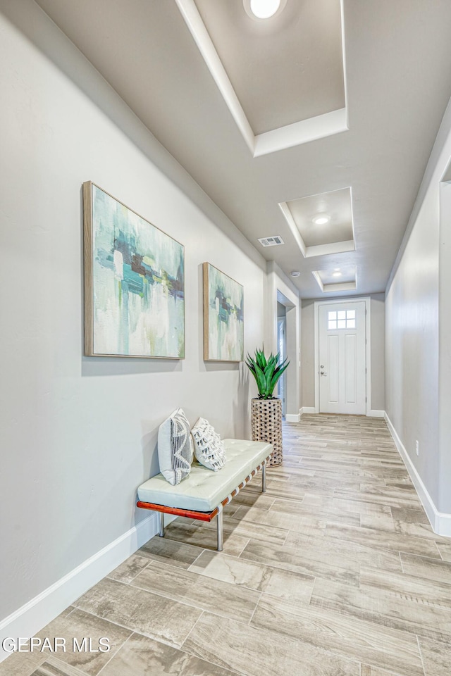 hallway featuring a tray ceiling and light hardwood / wood-style flooring