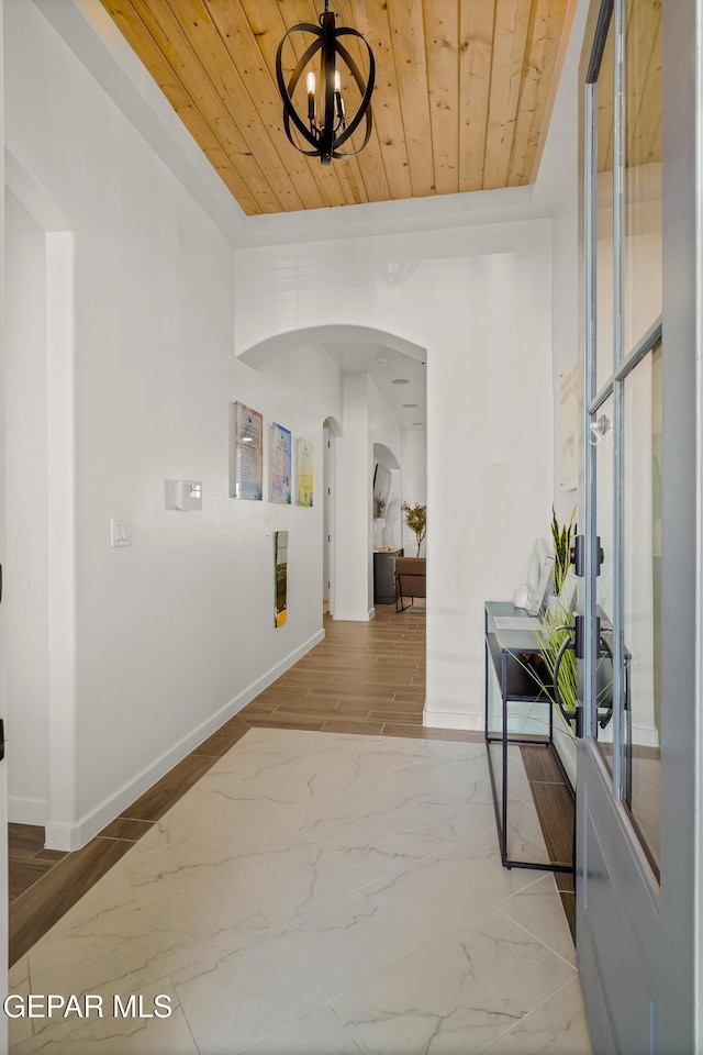 hallway featuring wood ceiling, arched walkways, and baseboards