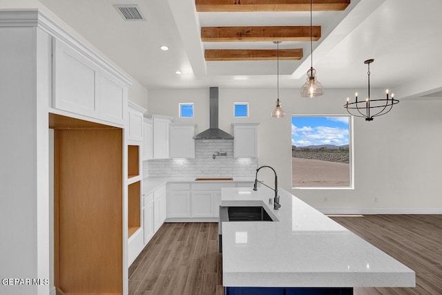 kitchen with tasteful backsplash, visible vents, wall chimney range hood, an island with sink, and a sink