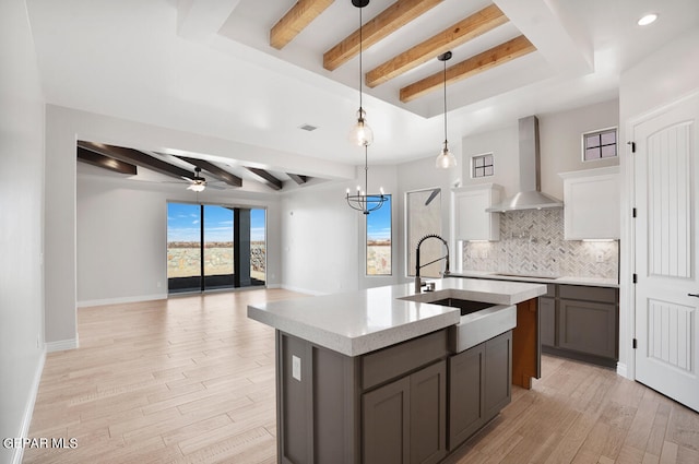 kitchen with wall chimney range hood, beam ceiling, white cabinets, and ceiling fan with notable chandelier