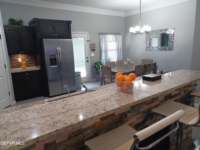 kitchen with stainless steel fridge, pendant lighting, a notable chandelier, backsplash, and sink