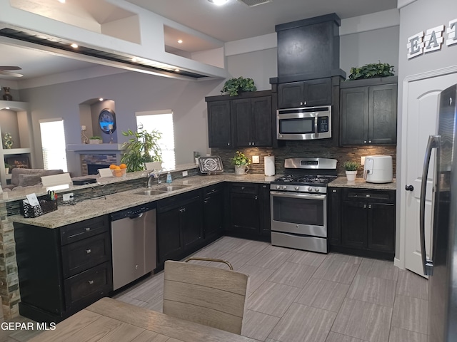 kitchen with a fireplace, stainless steel appliances, kitchen peninsula, sink, and decorative backsplash