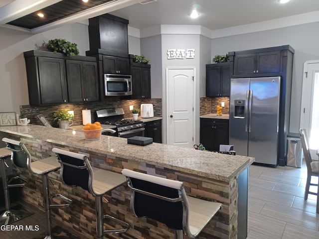 kitchen featuring a kitchen breakfast bar, backsplash, appliances with stainless steel finishes, kitchen peninsula, and light tile patterned flooring