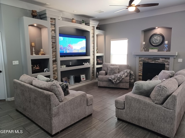 living room featuring built in shelves, ceiling fan, and a stone fireplace